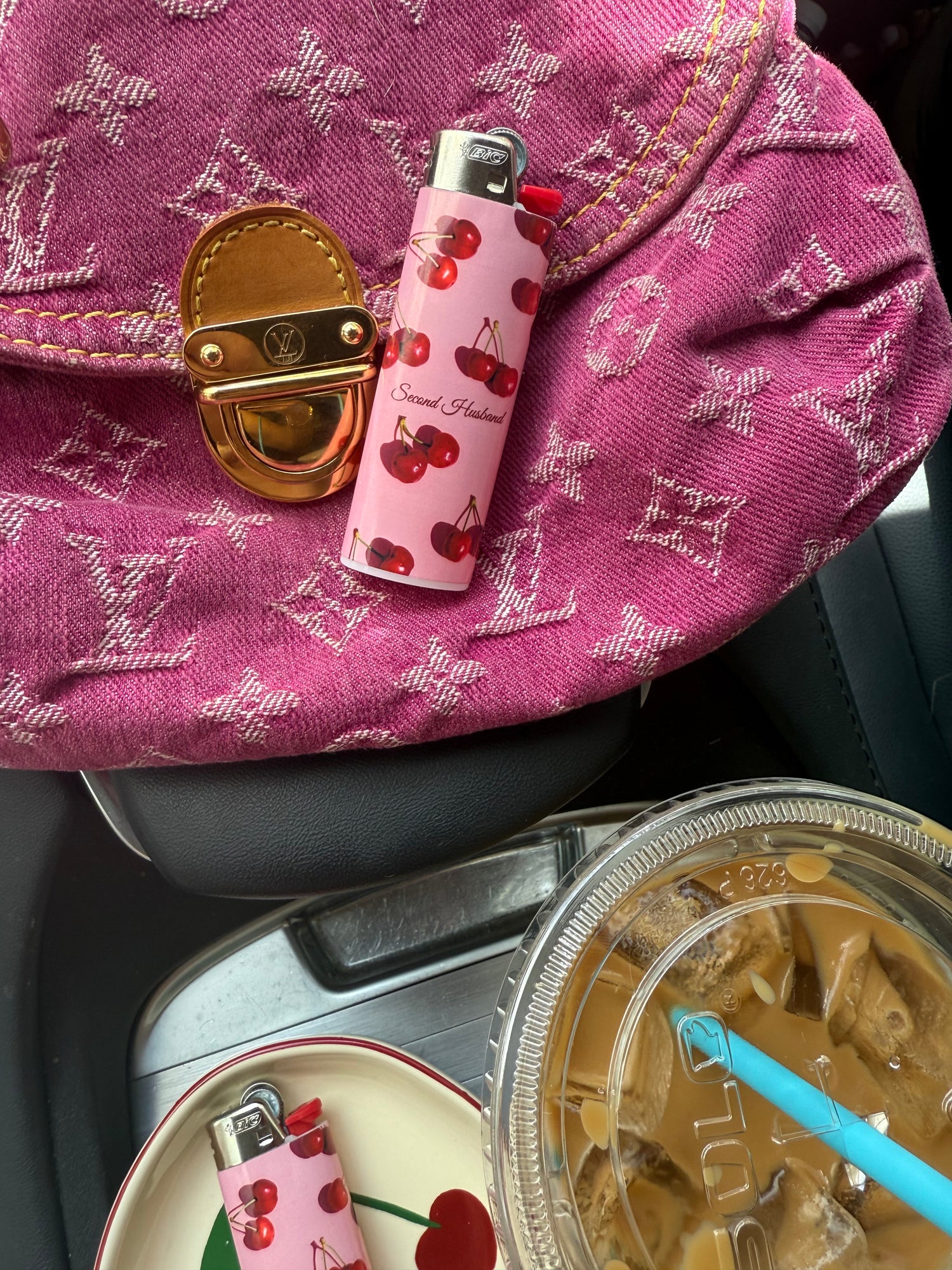 Pink patterned bag with a pink lighter and gold lock next to a cup of coffee.
