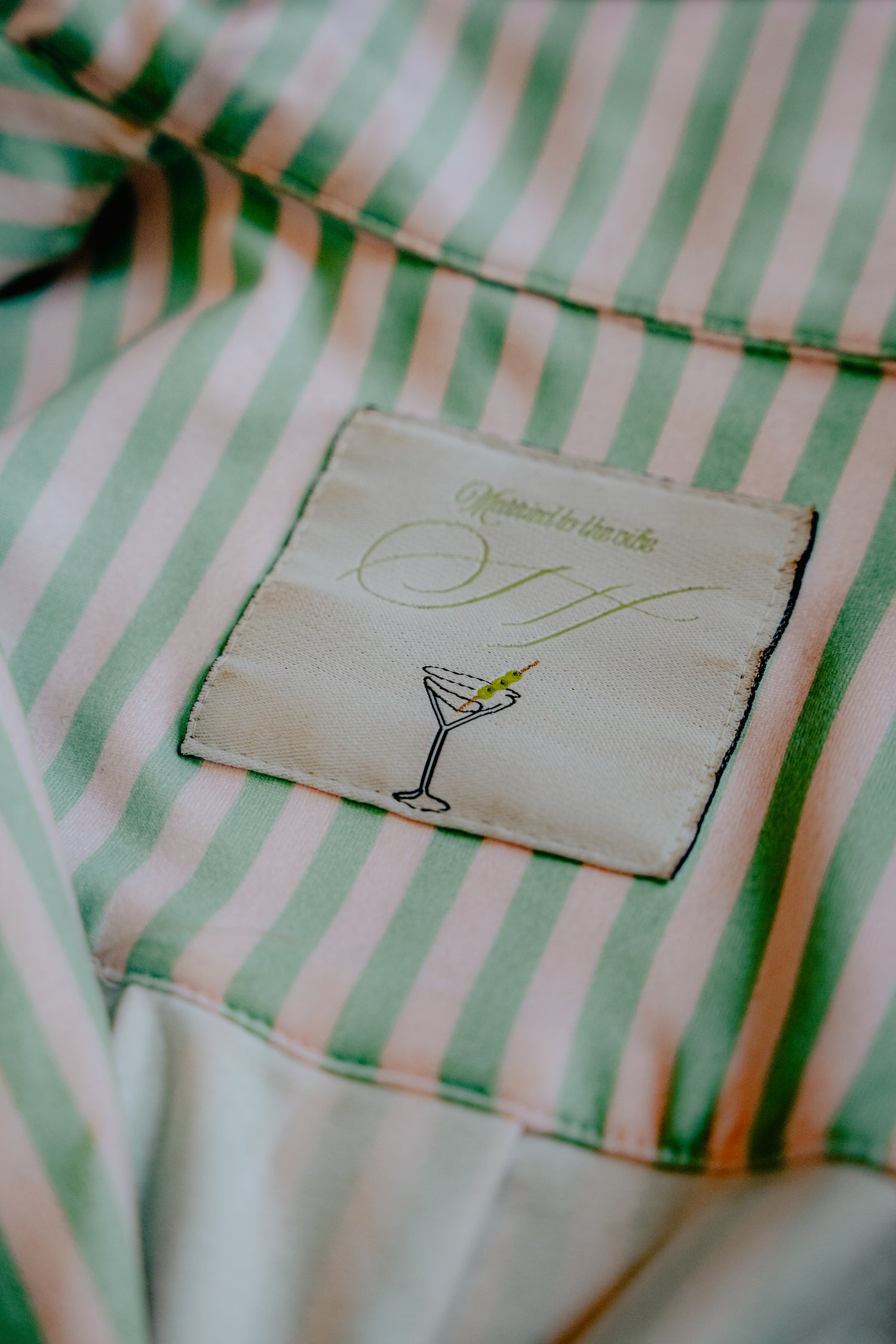 Close-up of a green and white striped shirt with a label featuring a cocktail illustration.