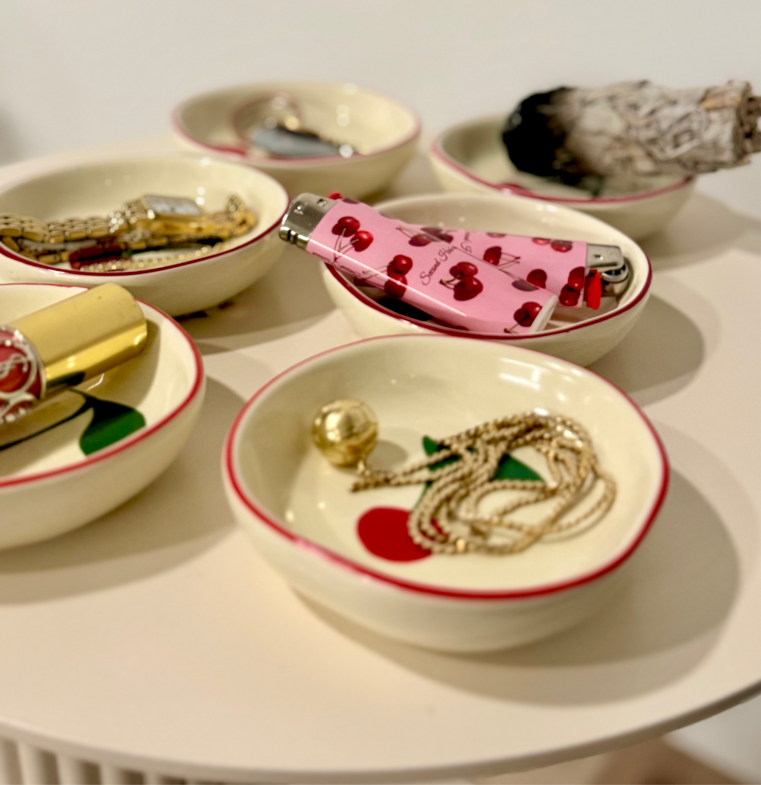 Set of small white bowls with red rims, each containing different jewelry items on a white surface.