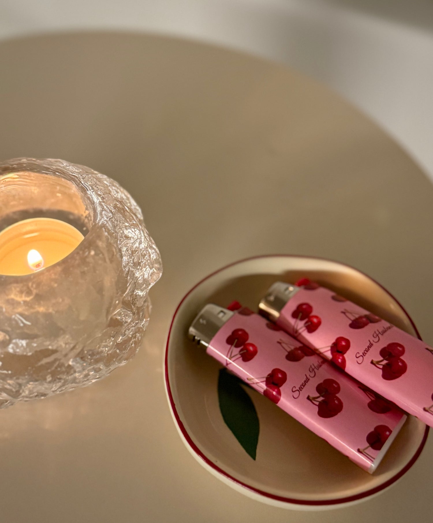 Pink chocolate bars with cherry design on a white plate next to a lit candle in a glass holder.