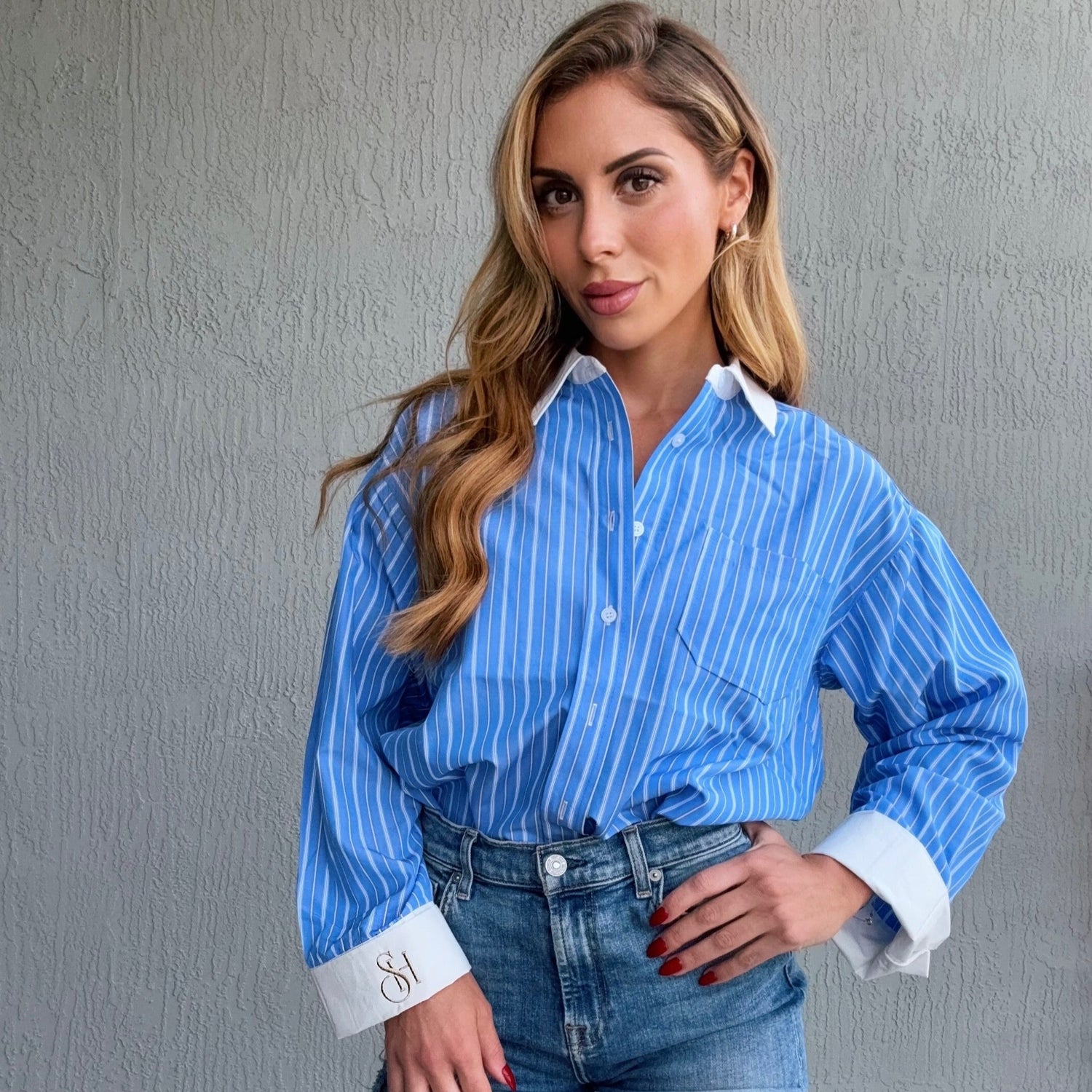 Woman wearing a blue striped shirt and denim shorts against a gray wall.