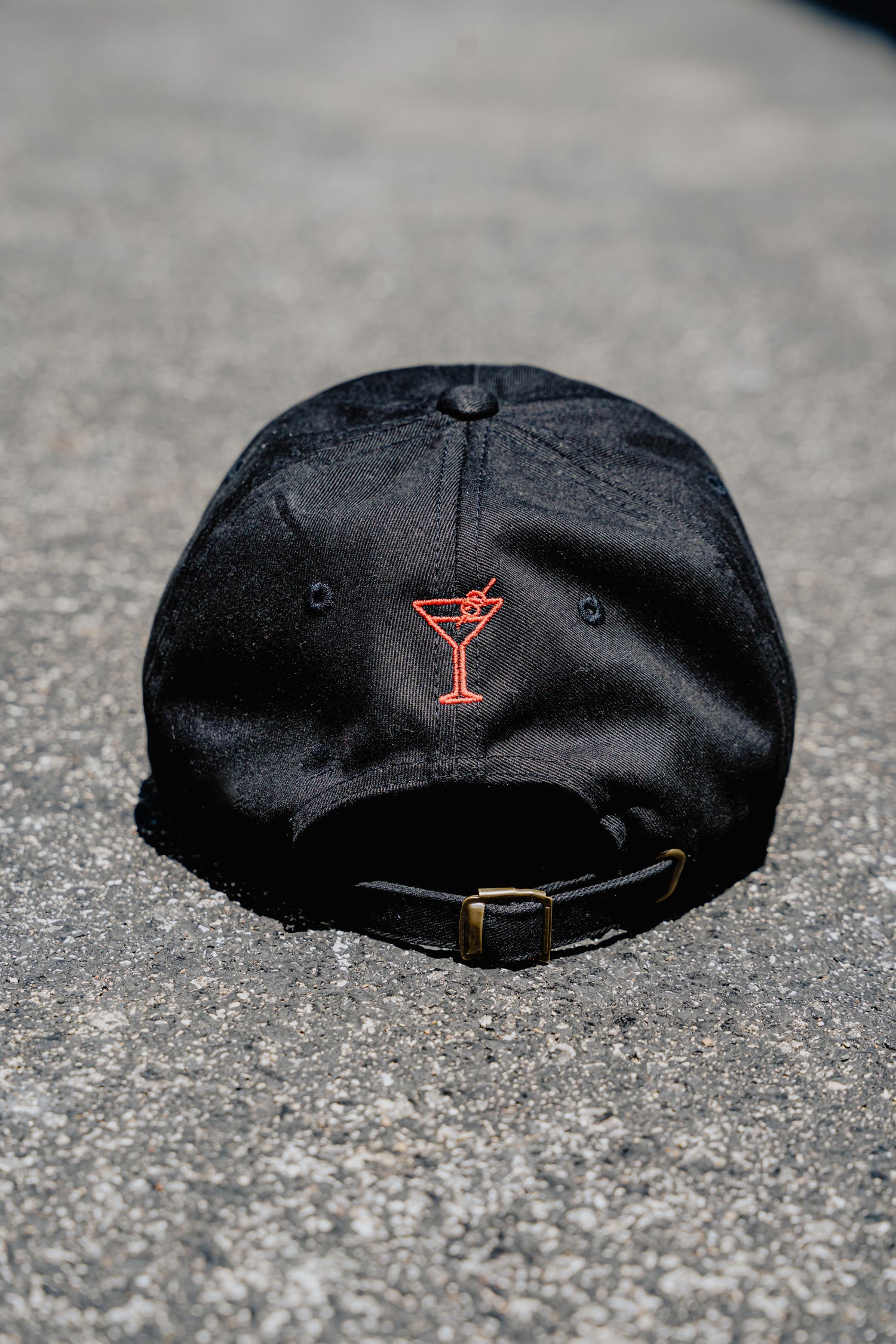 Black cap with a red martini glass logo on a gray surface