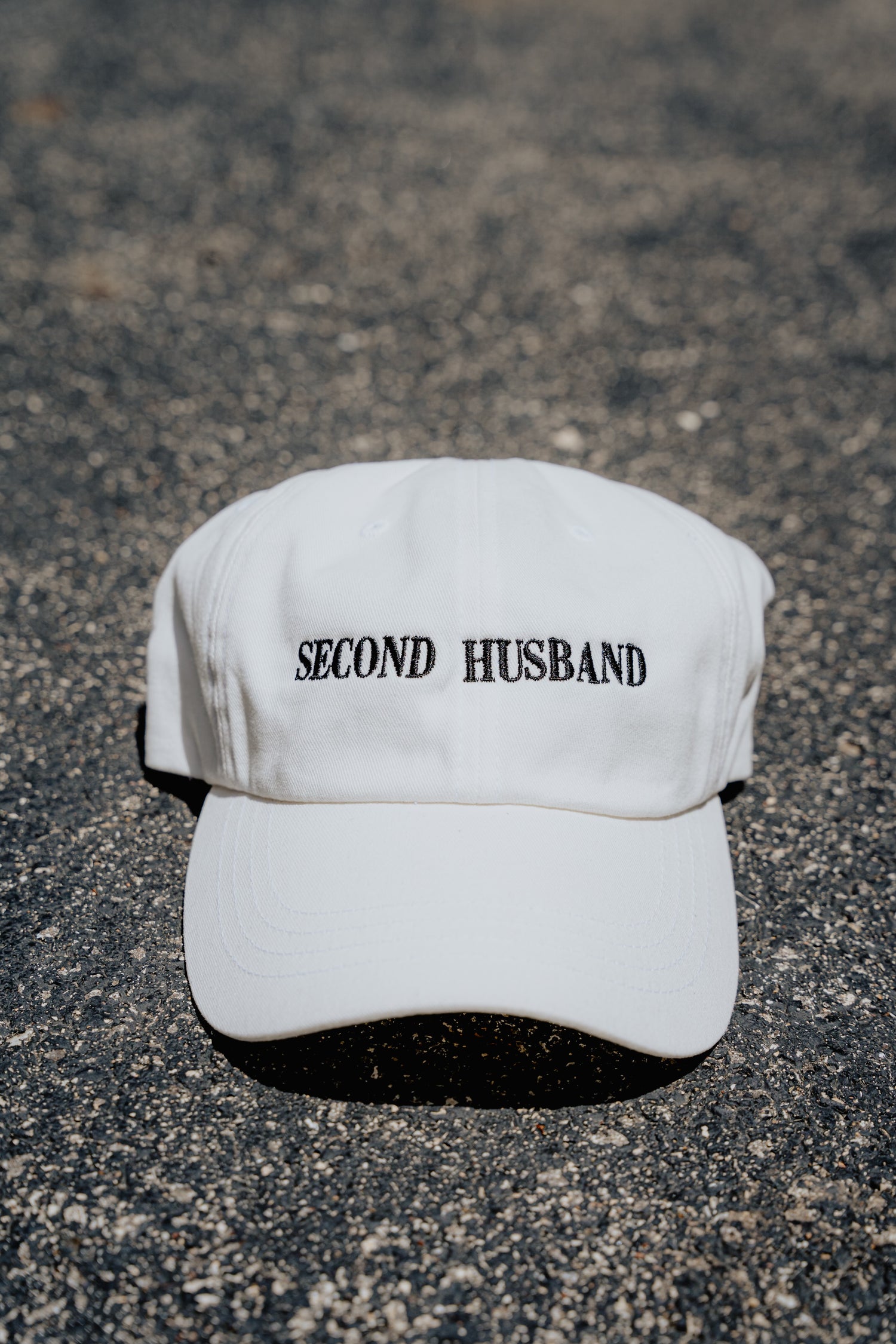 White cap with 'SECOND HUSBAND' text on a textured surface