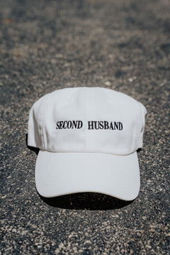 White cap with 'SECOND HUSBAND' text on a textured surface