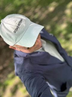 Person wearing a white cap with 'Second Husband' text, outdoors.