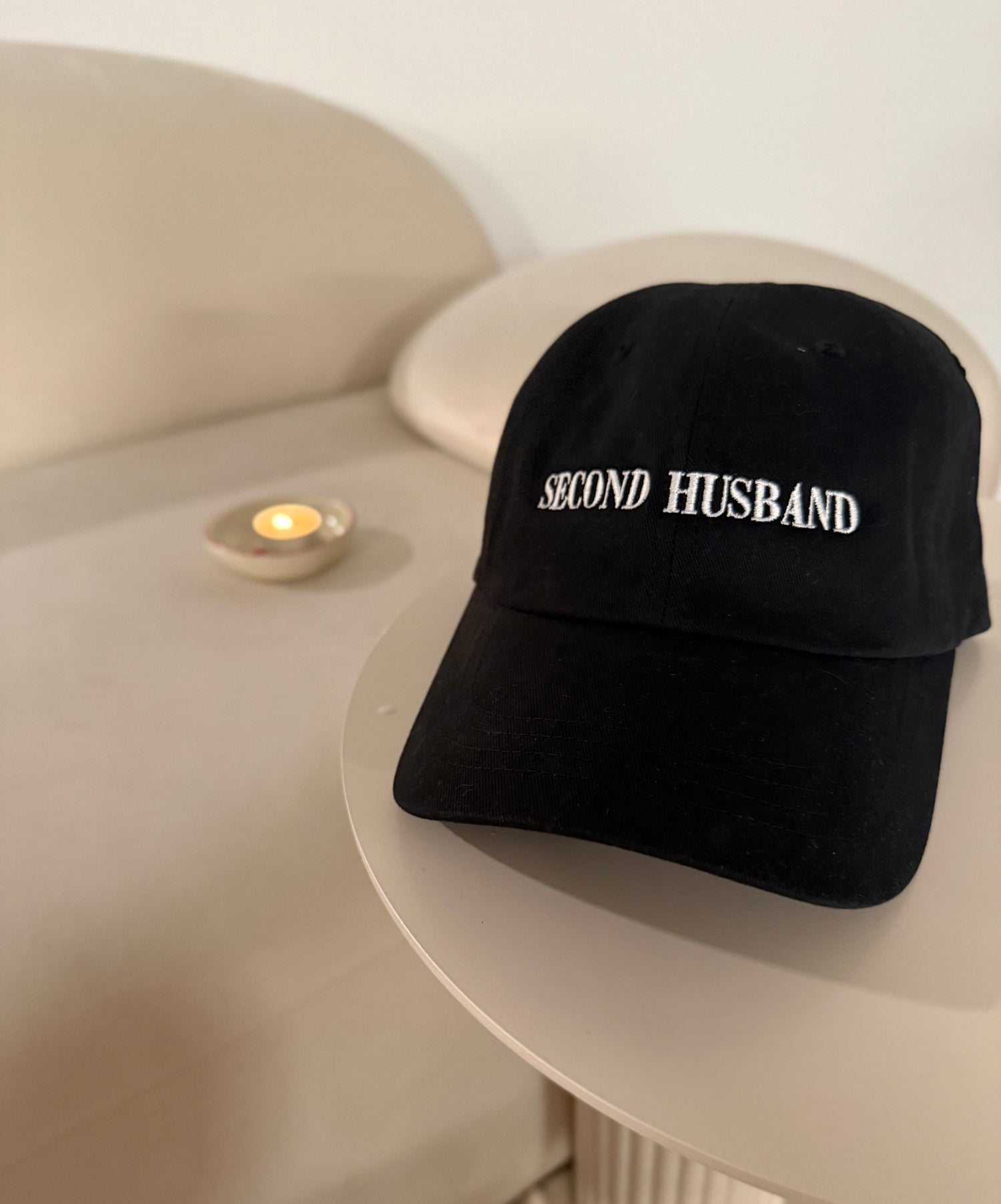 Black cap with 'SECOND HUSBAND' text on a white surface